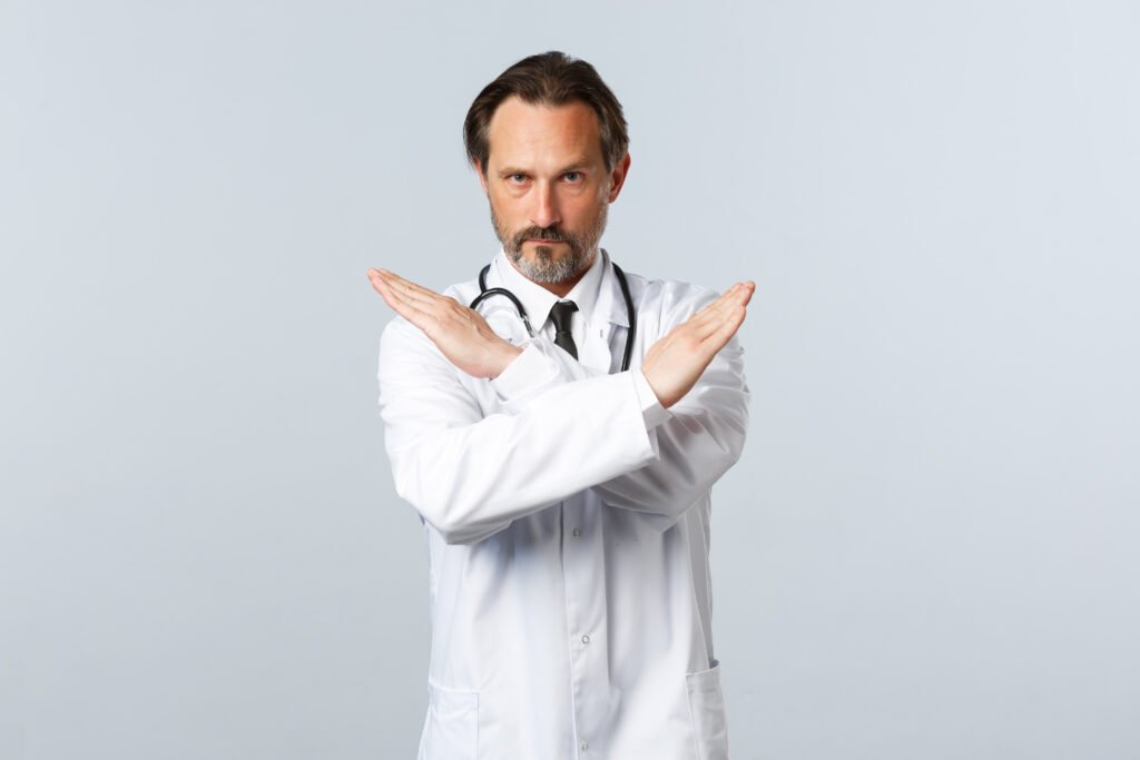 covid 19, coronavirus outbreak, healthcare workers and pandemic concept. serious displeased male doctor in white coat, cross hands to show stop gesture, prohibit or forbid smth